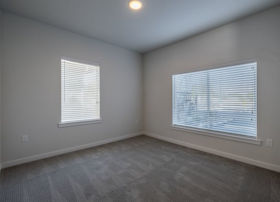 an empty living room with two windows and carpeting at Sagecrest Apartments, Washington