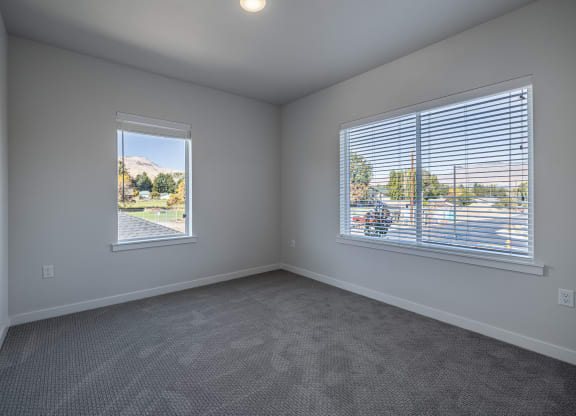 an empty living room with two windows and carpeting at Sagecrest Apartments, Washington, 98801