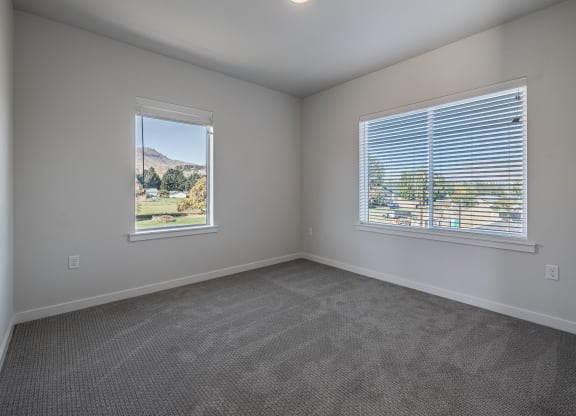 an empty living room with two windows and carpeting at Sagecrest Apartments, Washington