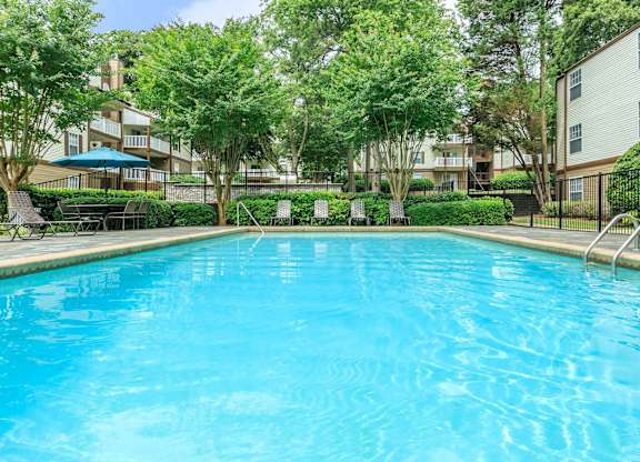 A swimming pool surrounded by trees and apartment buildings.