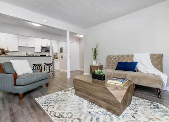 A modern living room with a grey sofa, a wooden coffee table, and a kitchen area in the background.
