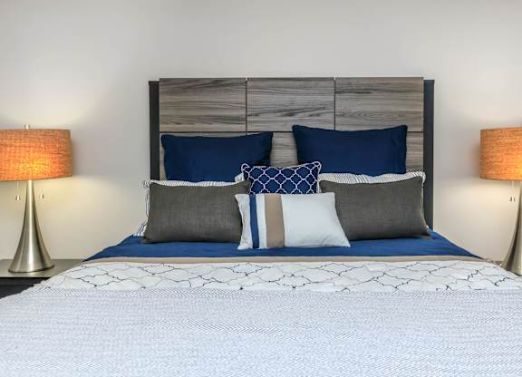 A bed with a white comforter and blue pillows is flanked by two lamps.