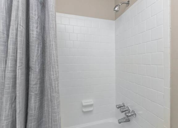 A white tiled shower with a grey curtain.