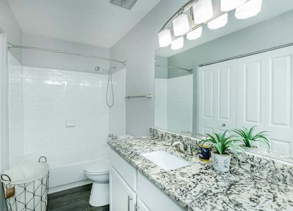 A bathroom with a marble countertop and white fixtures at Crest at East Cobb Apartments, Georgia