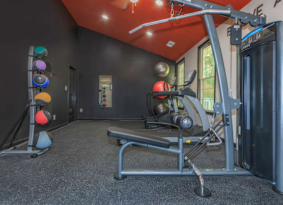 A gym with a rowing machine, a bench, and a set of dumbbells at Crest at East Cobb Apartments, Marietta, GA, 30062