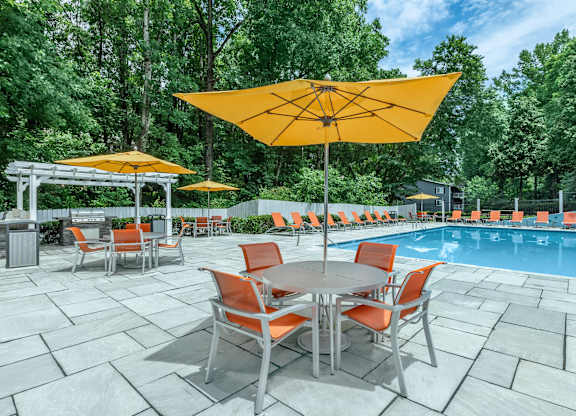 A poolside table with chairs and umbrellas is set up next to a pool at Crest at East Cobb Apartments, Marietta