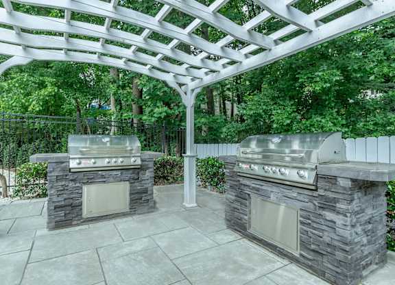 A patio with two grills under a white pergola at Crest at East Cobb Apartments, GA, 30062