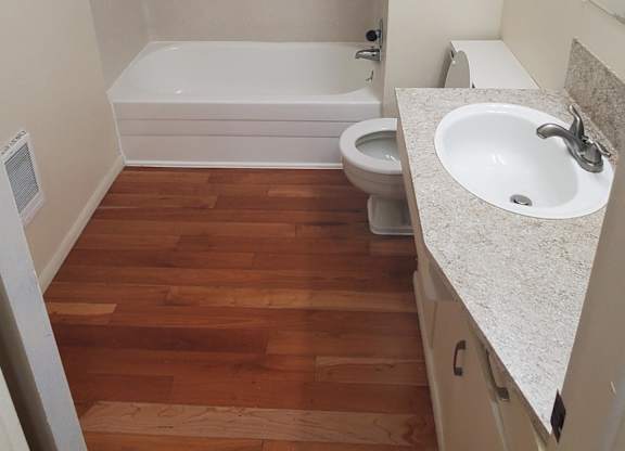 A white bathroom with a wooden floor and a white tub.