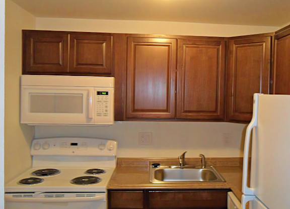 A kitchen with a white refrigerator, white stove, and brown cabinets.