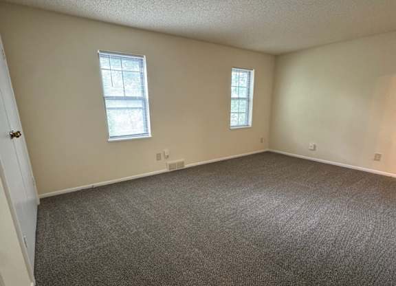 A room with carpeted floor and two windows.