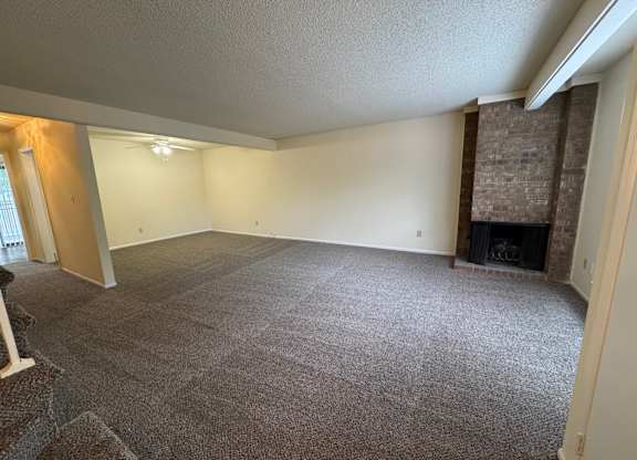 A large, empty room with a fireplace and a carpeted floor.