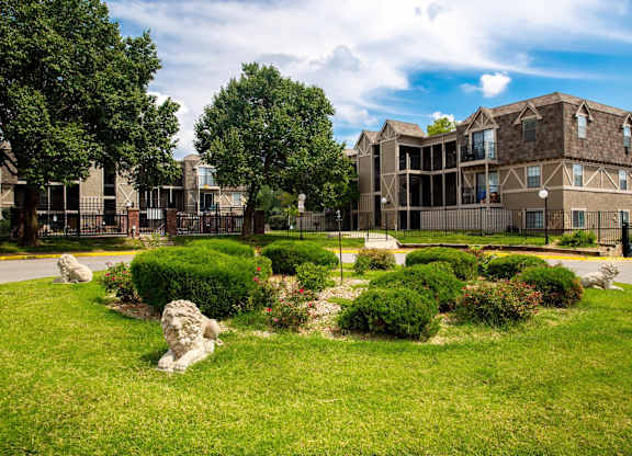 A stone lion statue sits in a green grassy area in front of a building.