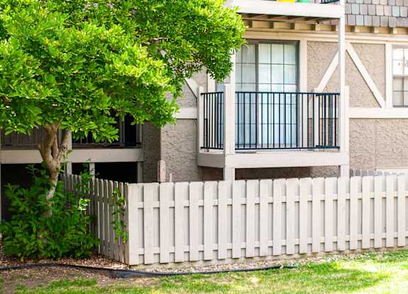 A white picket fence in front of a building with a tree growing over it.