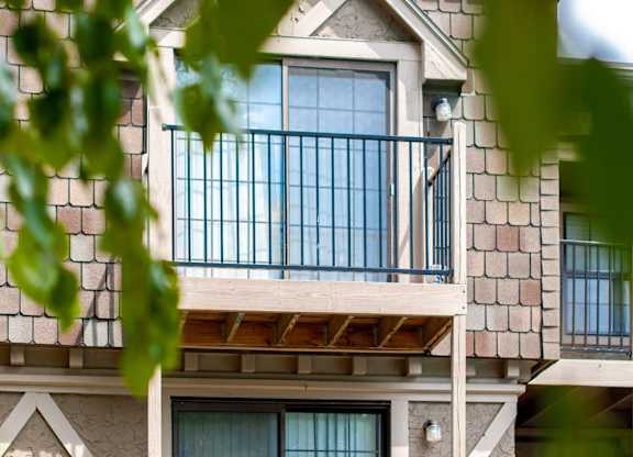 A balcony with a railing and a window is seen through the leaves.