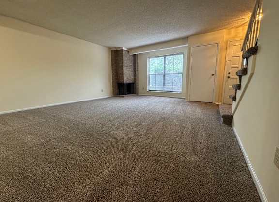 A carpeted room with a staircase on the right side.