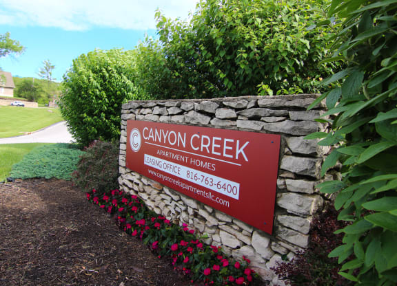 a sign for canyon creek elementary homes in front of a stone wall and plants