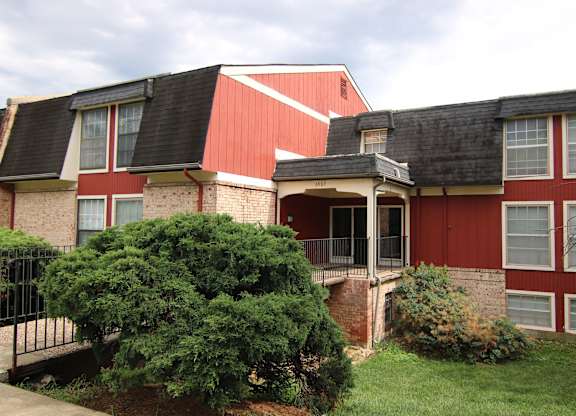 A red and white house with a black roof and a green bush in front.
