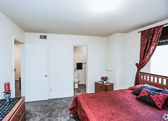 a bedroom with a red bed and a bathroom with a toilet at Gatehouse Apartments, Missouri, 64134
