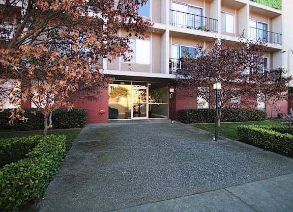 A building with a red door and windows is surrounded by trees and bushes.