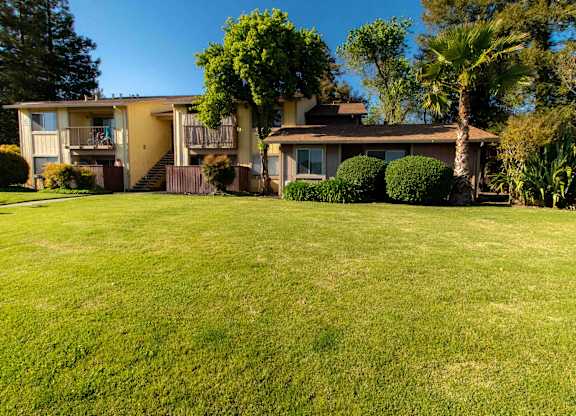A large grassy area in front of a two story house with a tree in front of the house.