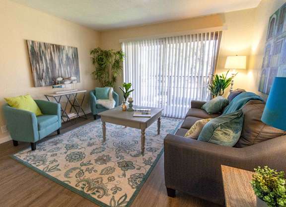 A living room with a rug, a sofa, a chair, a coffee table, and a potted plant.
