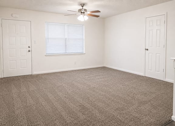 A room with a carpeted floor, a ceiling fan, and two doors.