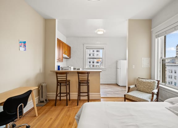 a bedroom with a bed and a kitchen with a bar and a large window