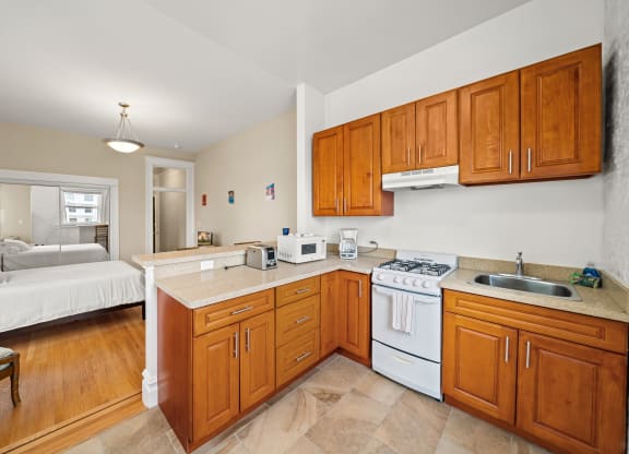 a kitchen with wooden cabinets and white appliances and a bedroom with a bed