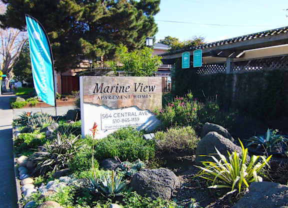 A sign for Marine View Apartment Homes is in front of a fence.