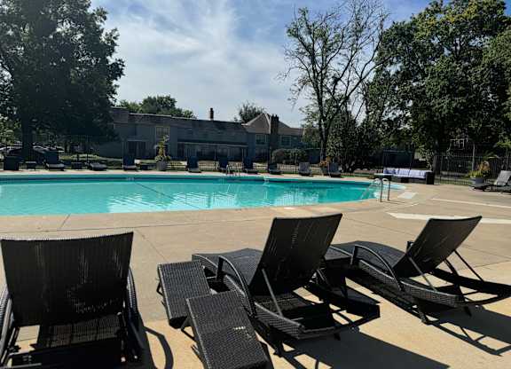A pool surrounded by trees and chairs.