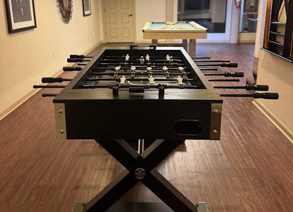 A foosball table in the middle of a room with wood flooring and white walls.