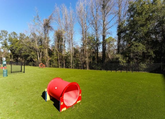 a red trash can sitting on top of a lush green field  at Fusion, Jacksonville, FL, 32256