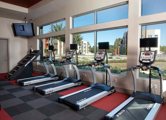 a room with a row of treadmills and a treadmill in front of a large window  at Luxor Club, Jacksonville, FL, 32258