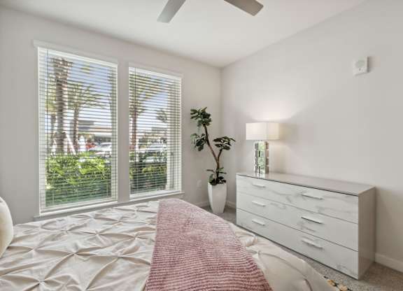 A bedroom with a bed, dresser, and window with blindsat Pinnacle Apartments, Jacksonville, FL