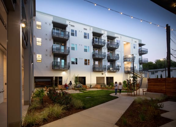 Interior courtyard at dusk with lighted balconies and walkways, showing green courtyard and walking path.