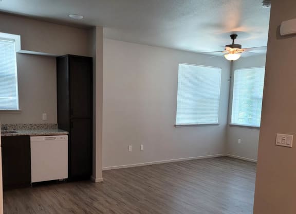 Living room and partial kitchen at Lavender with wood floors, dark cabinets, and white dishwasher. room at overhead lights and windows.