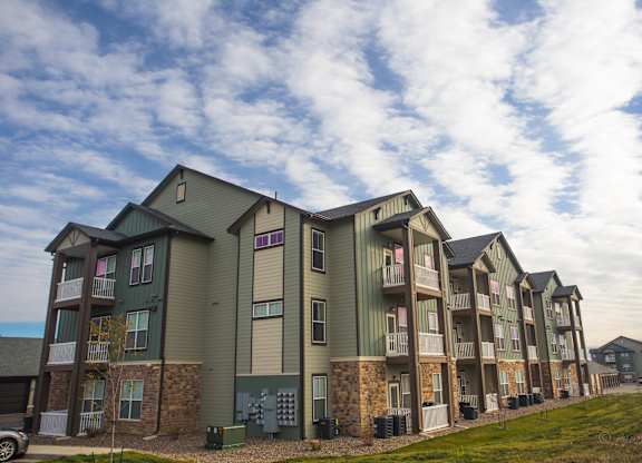Apartment complex with green and brown buildings and a cloudy sky.