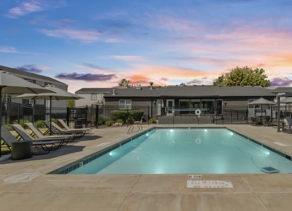 Proximity Apartment Homes pool with chairs and umbrellas and a building with a sunset behind it