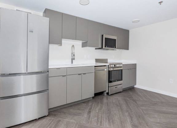 A modern kitchen with stainless steel appliances and wooden flooring.