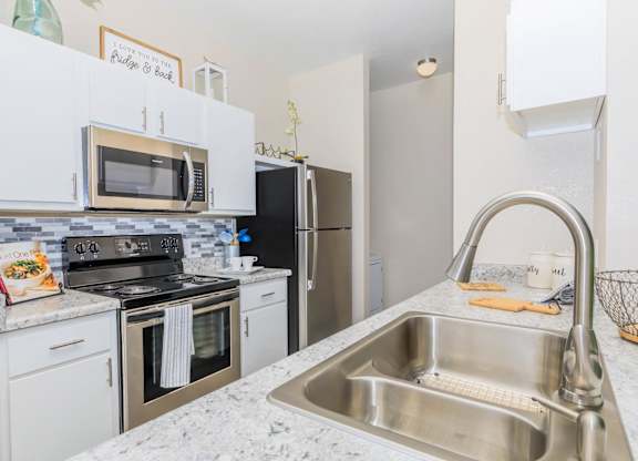 A kitchen with a stainless steel sink and white cabinets.