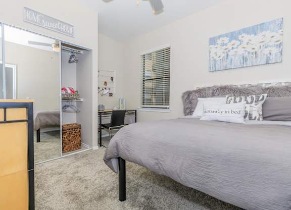 A bedroom with a bed, desk, and a mirrored closet.