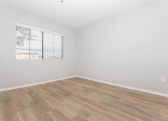 A room with wooden flooring and a window with blinds.