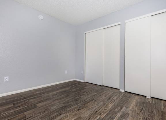 A room with white walls and wood flooring with three white closet doors.