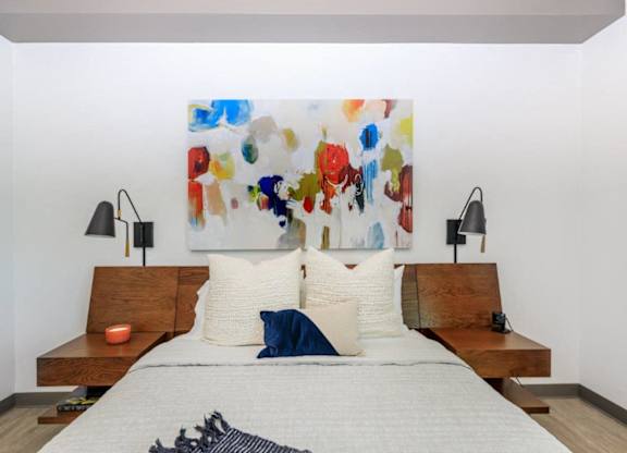 A bedroom with a large painting on the wall and a bed with white bedding.