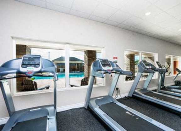 A gym with treadmills and a view of a pool outside the window.
