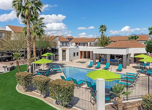 A pool area with a green umbrella and blue chairs.