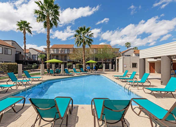 A pool surrounded by lounge chairs and palm trees.