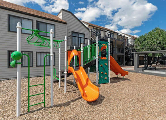 A playground with a green ladder, a green and orange slide, and a green and orange climbing structure.