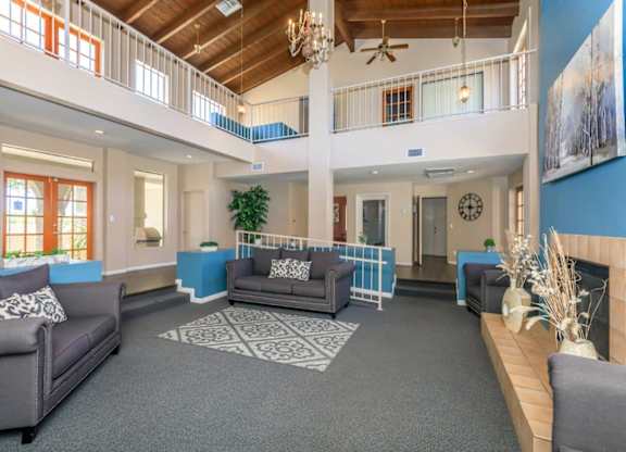 A large open living room with a grey carpet and a grey couch.