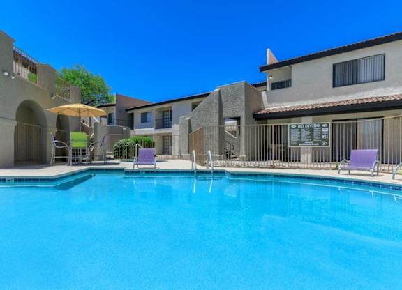 A swimming pool in front of a building with a sun lounger and umbrella.